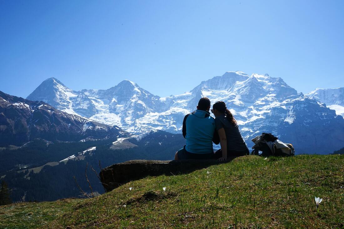 A couple sitting in the grass with mountains in the background.