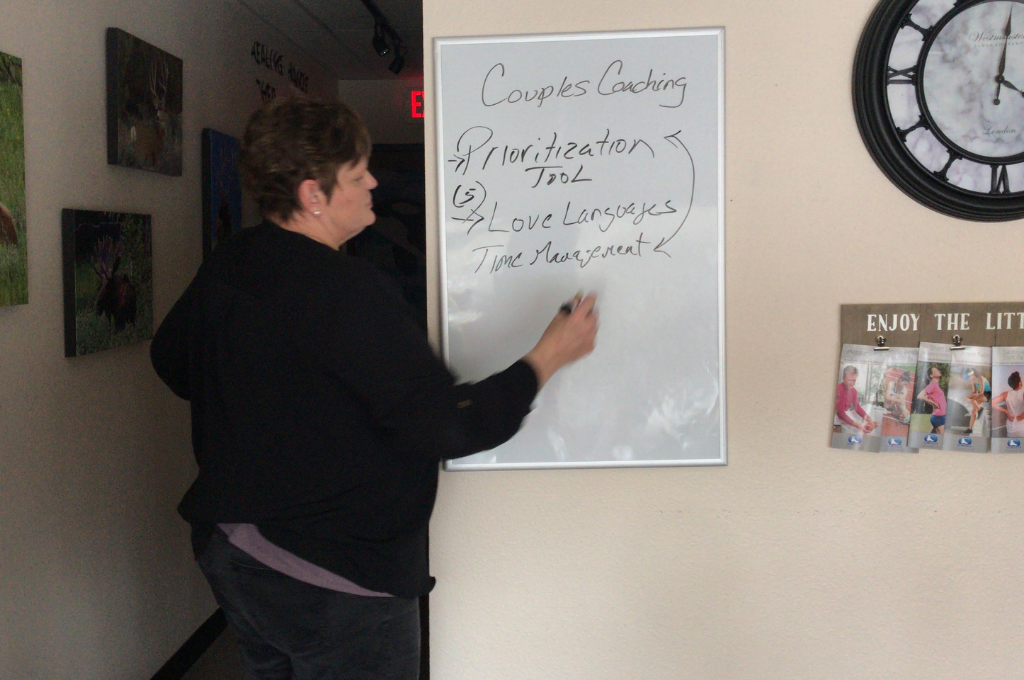 Laura Pollard in front of white board showing a list of activities for couples coaching